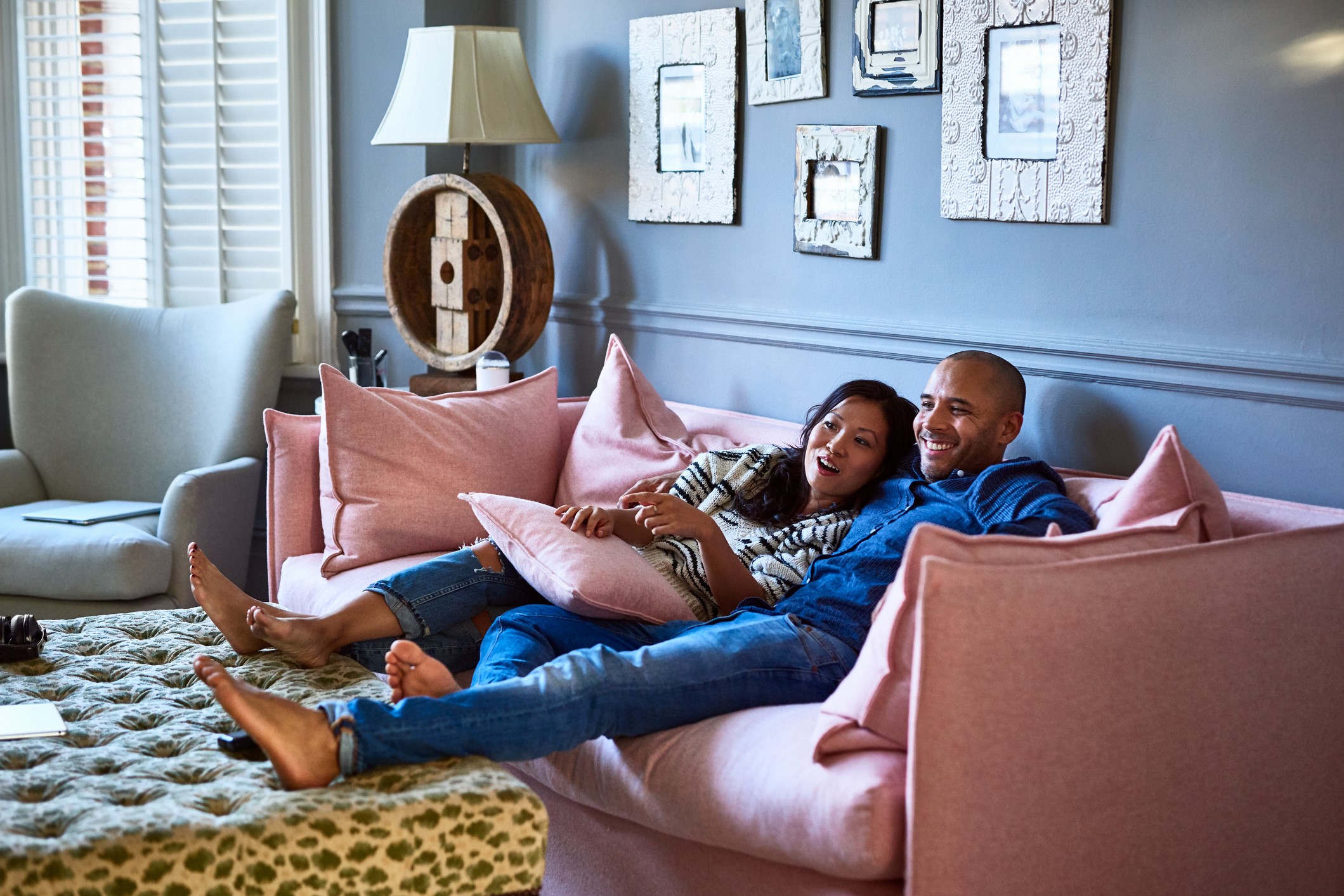 A man with his arm around a woman, sitting with their feet up on a pink sofa, smiling.