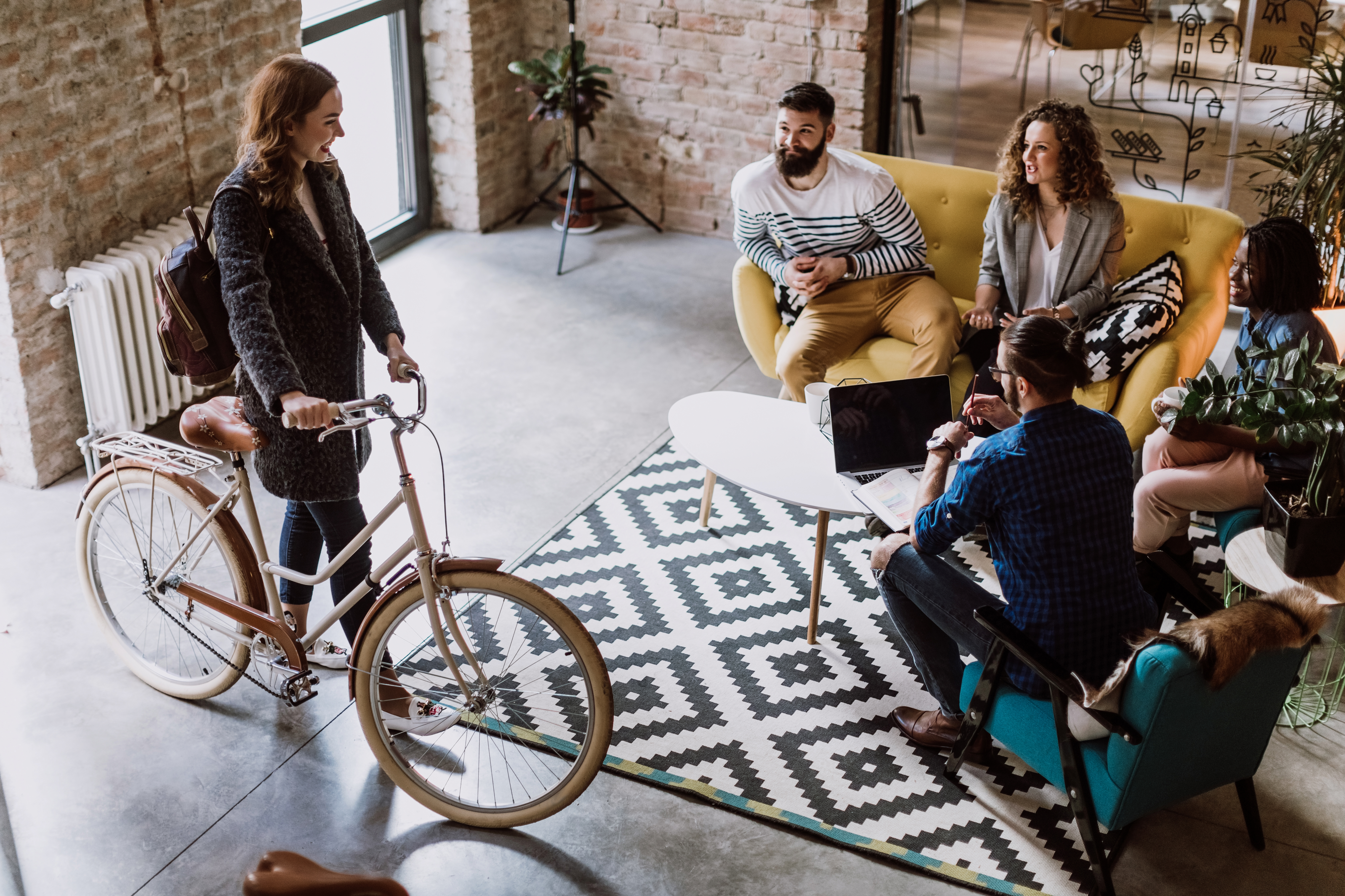 A young woman arrives at a office by bicycle and greets her colleagues.