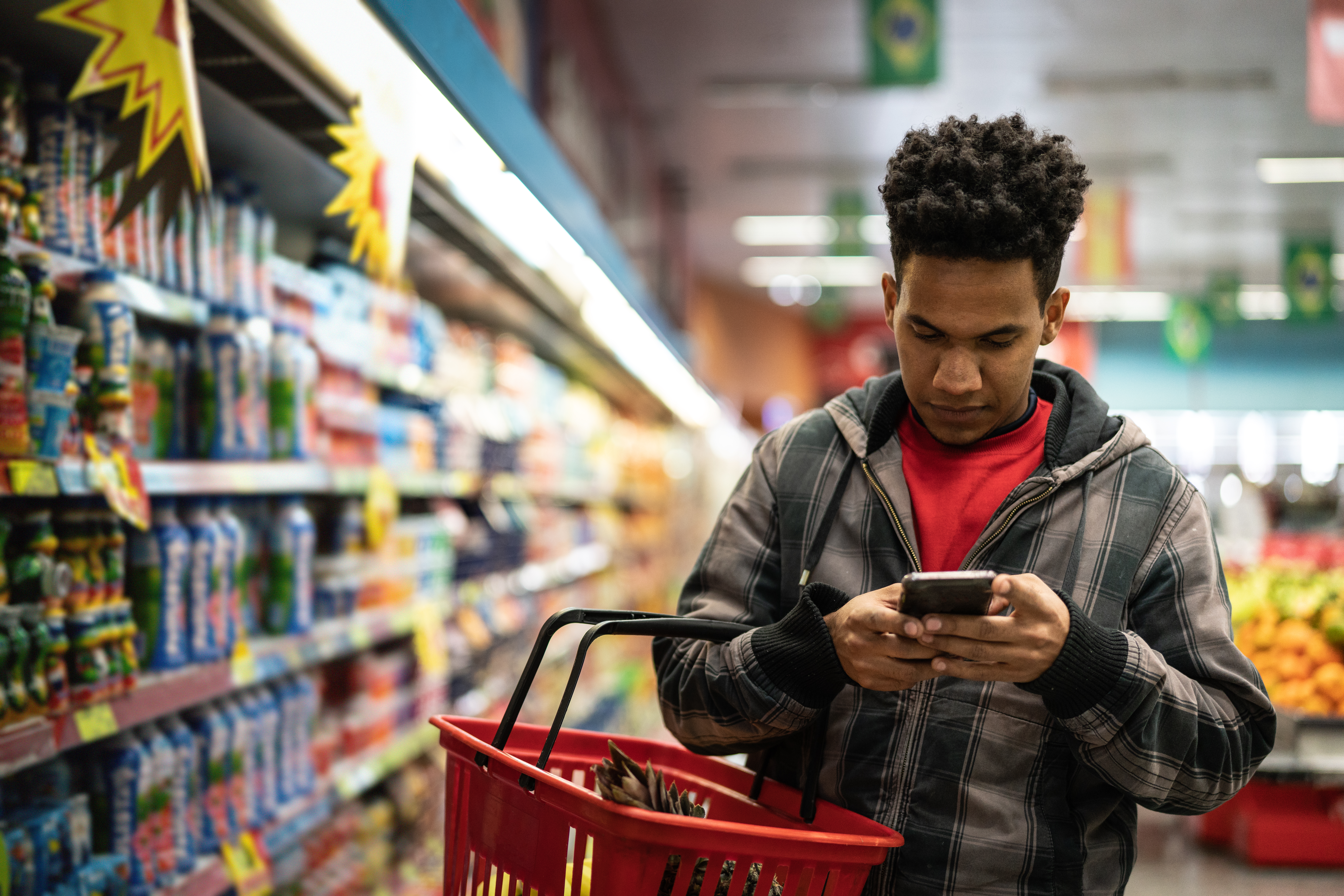 A man looks at his phone as he shops in a supermarket.
