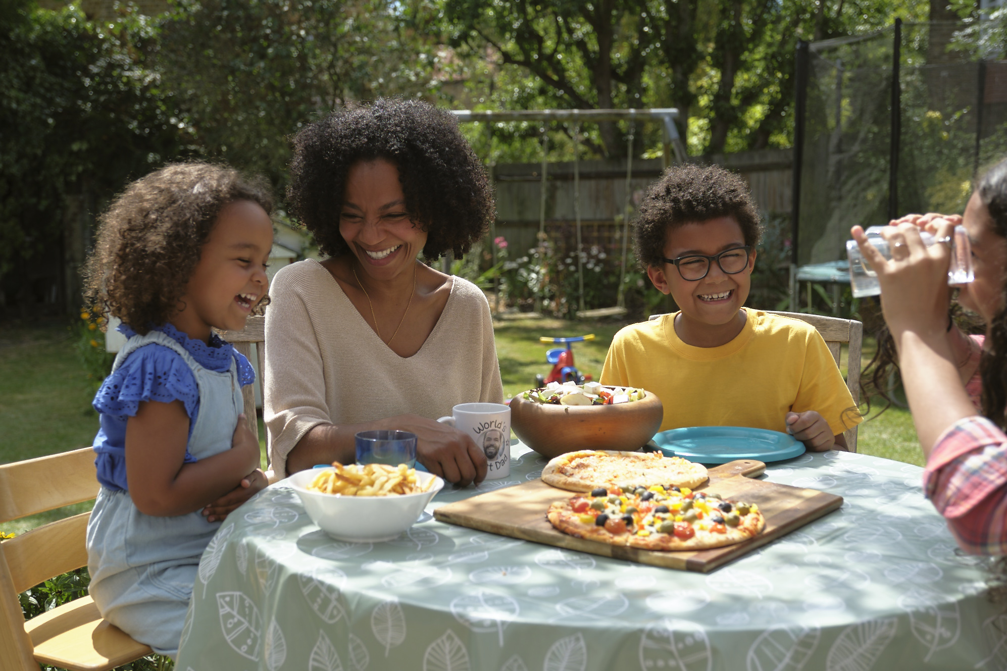 A family enjoying dinner outdoors at a garden table and chairs, in the sunshine with smiles on their faces.