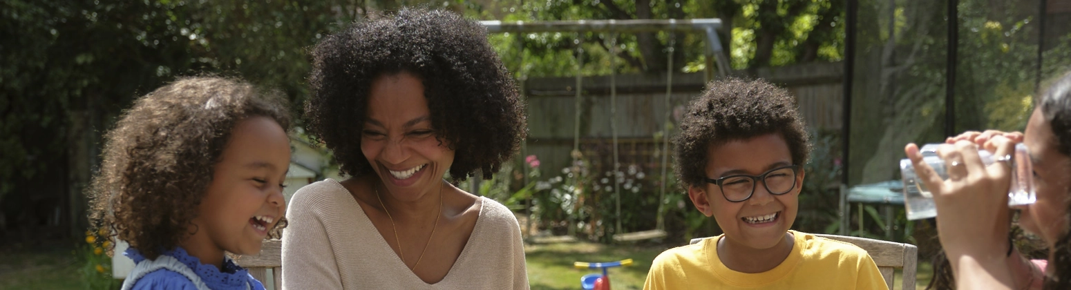 A family enjoying dinner outdoors at a garden table and chairs, in the sunshine with smiles on their faces. A family enjoying dinner outdoors at a garden table and chairs, in the sunshine with smiles on their faces.