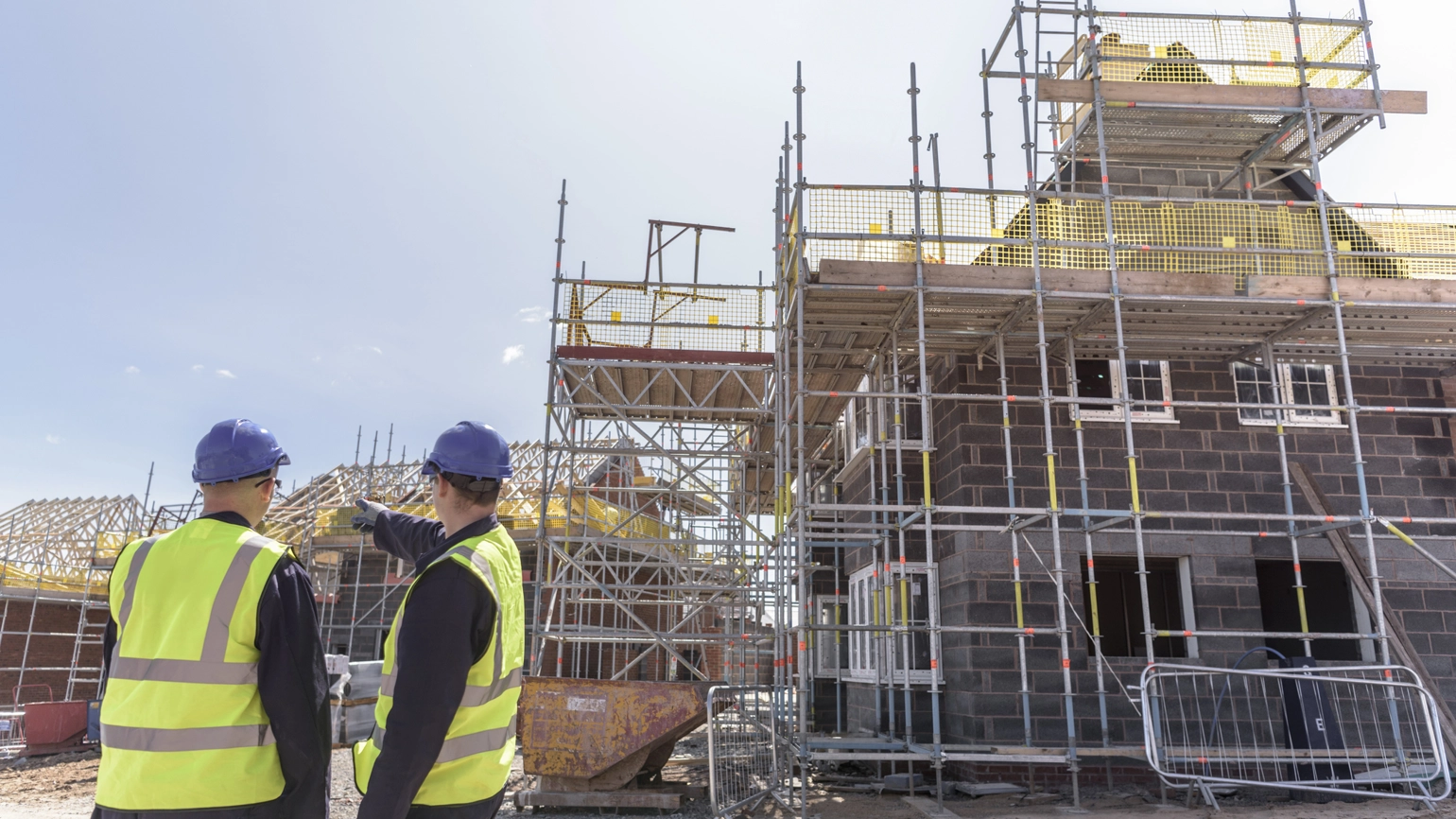 Two builders discuss a housing development on a building site. Two builders discuss a housing development on a building site.