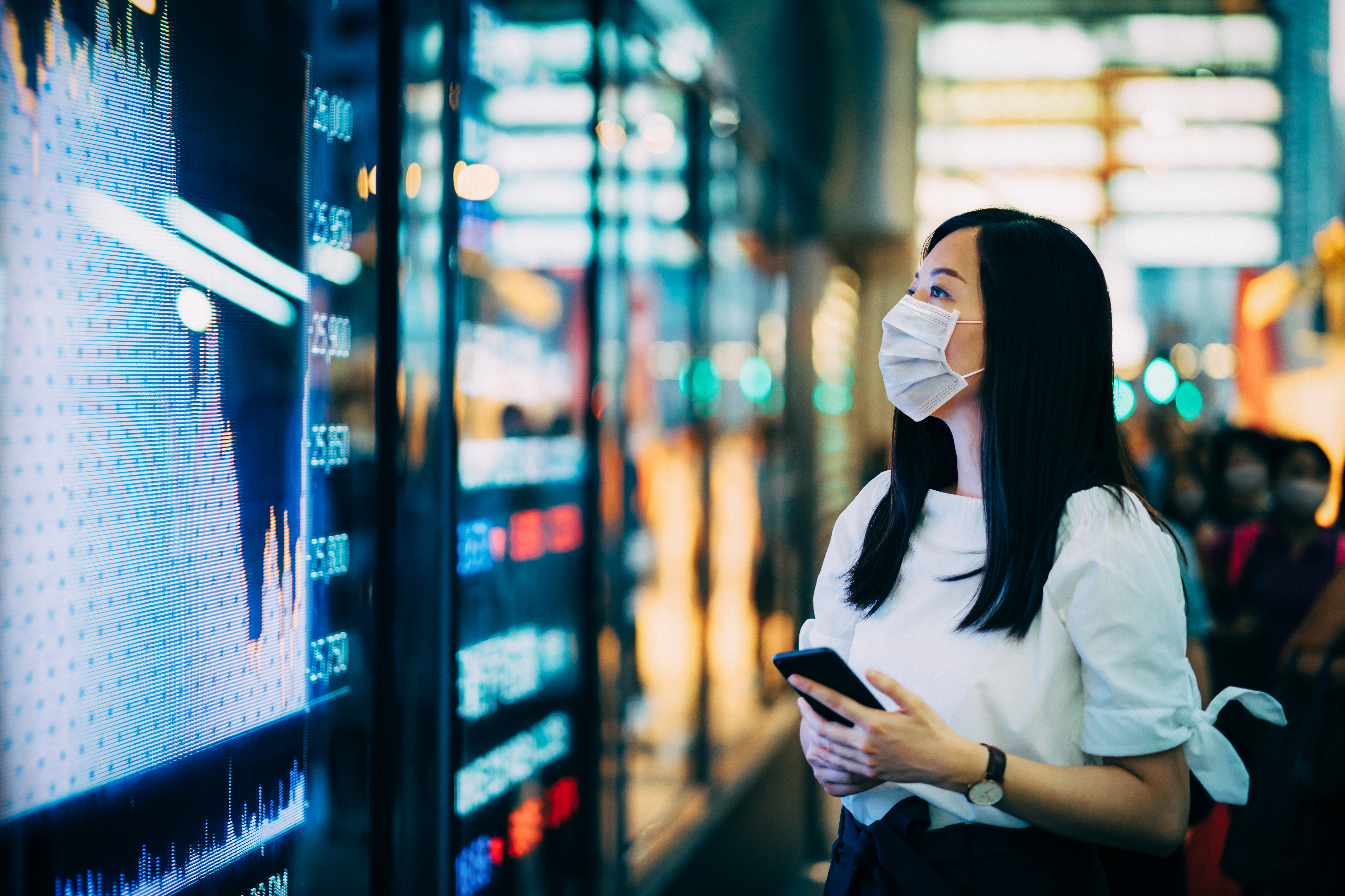 Female with face mask on checking stock charts in the street 